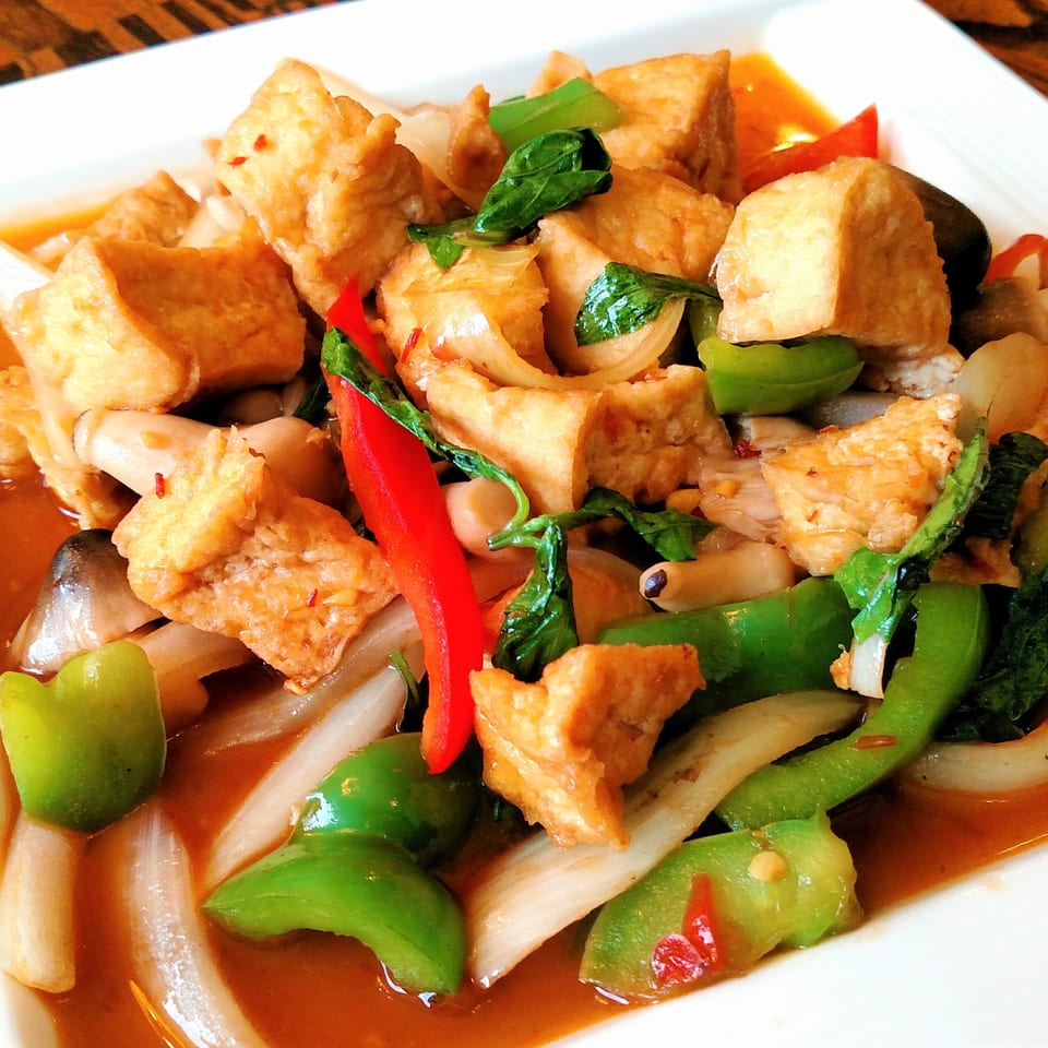 A vibrant Thai dish with crispy tofu, green peppers, red chilies, onions, and basil in a rich sauce.