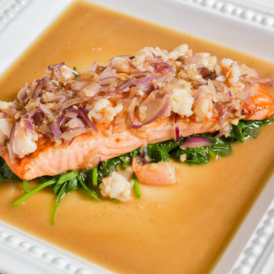 Salmon fillet topped with shrimp and red onions, served over spinach in a savory sauce.