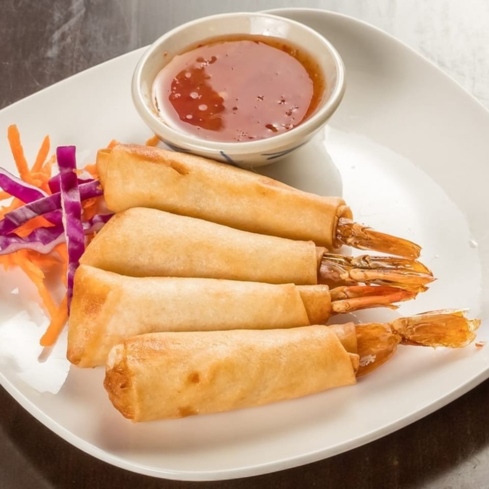 Four golden fried shrimp spring rolls with sweet chili sauce and shredded carrots and cabbage.