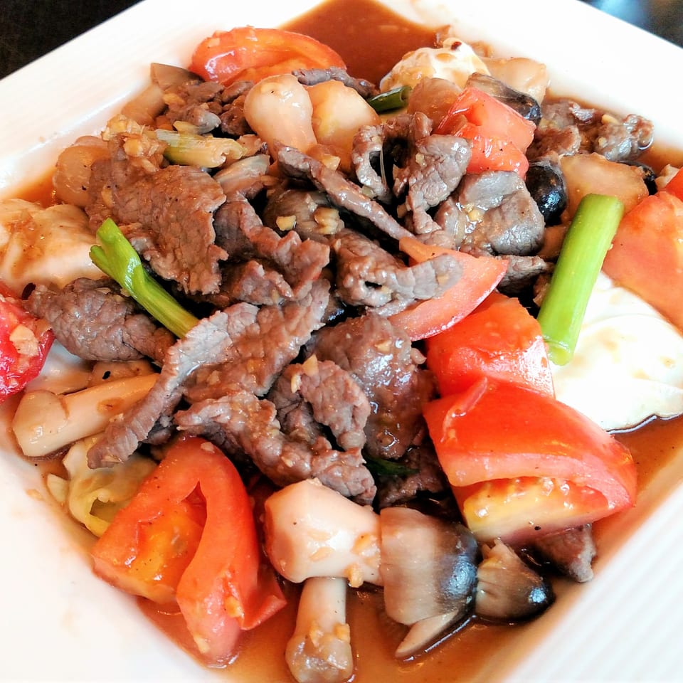Stir-fried beef with tomatoes, mushrooms, and green onions in a savory sauce on a white plate.